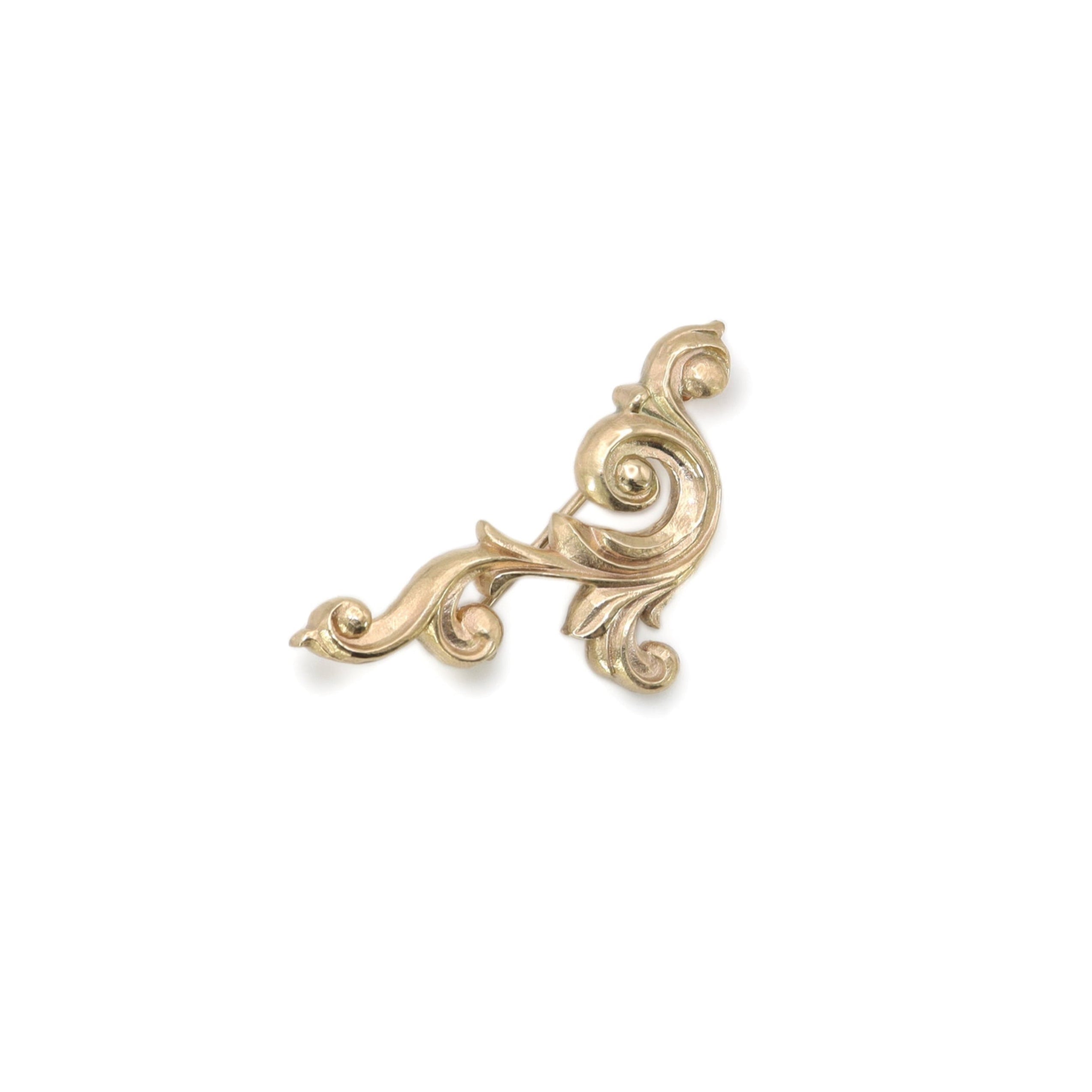 Gold decorative scroll brooch on a white background