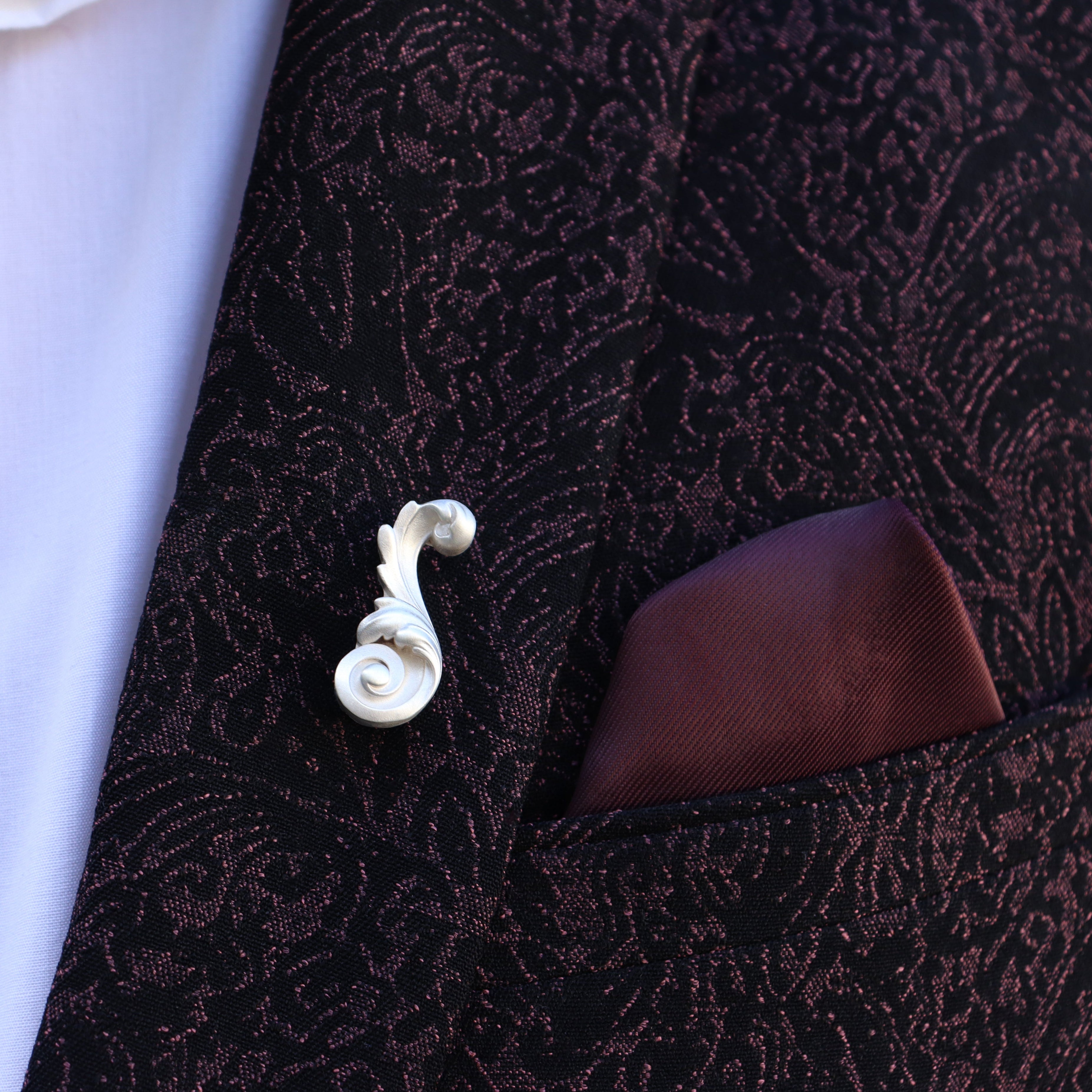 Close-up of a patterned suit jacket with a white shirt and decorative Acanthus Leaf lapel pin.